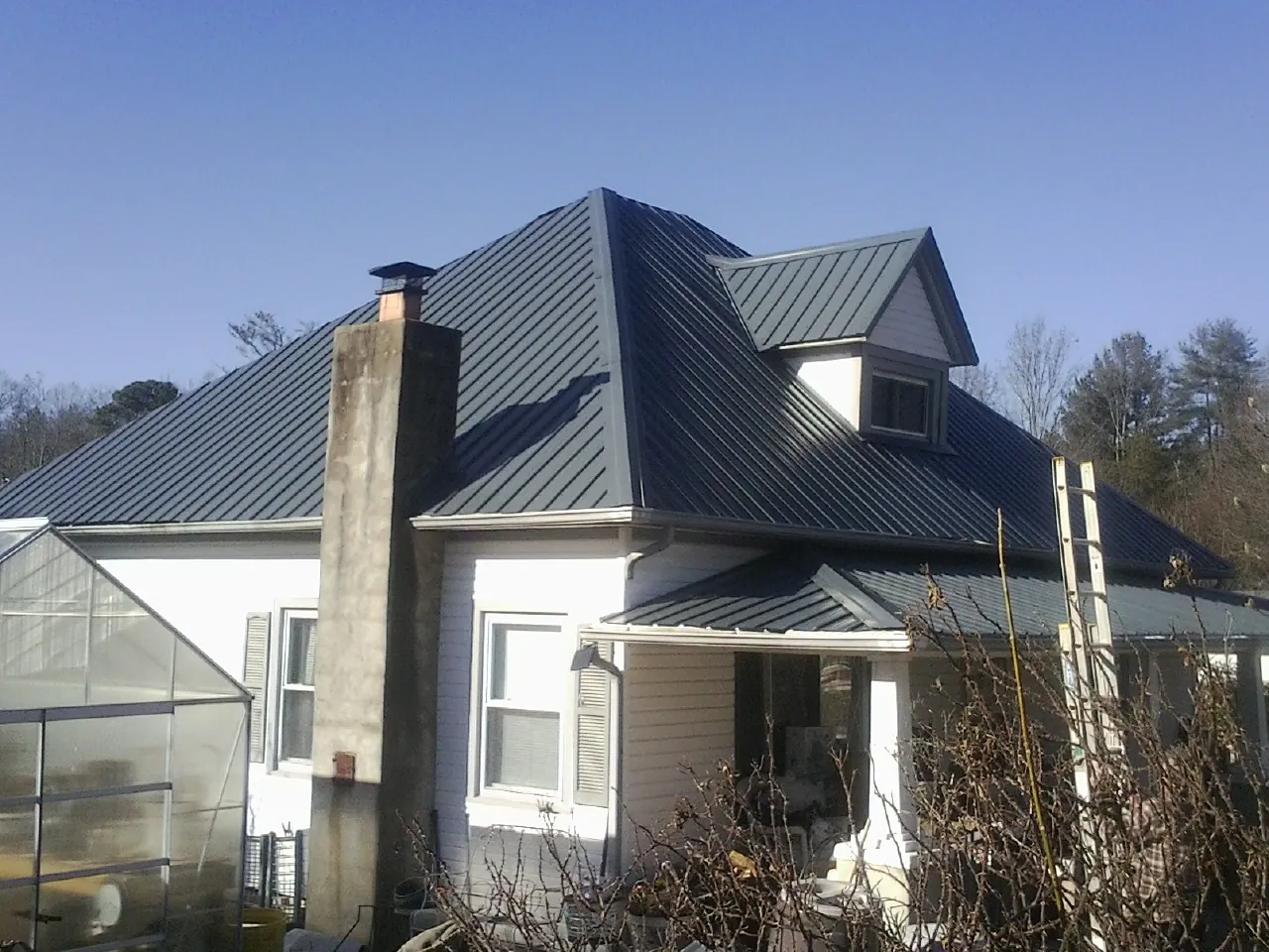 Dark blue standing seam metal roof on a white farmhouse with dormer — Slate & Tile Roof Repair by Roofing Brothers in Penryn