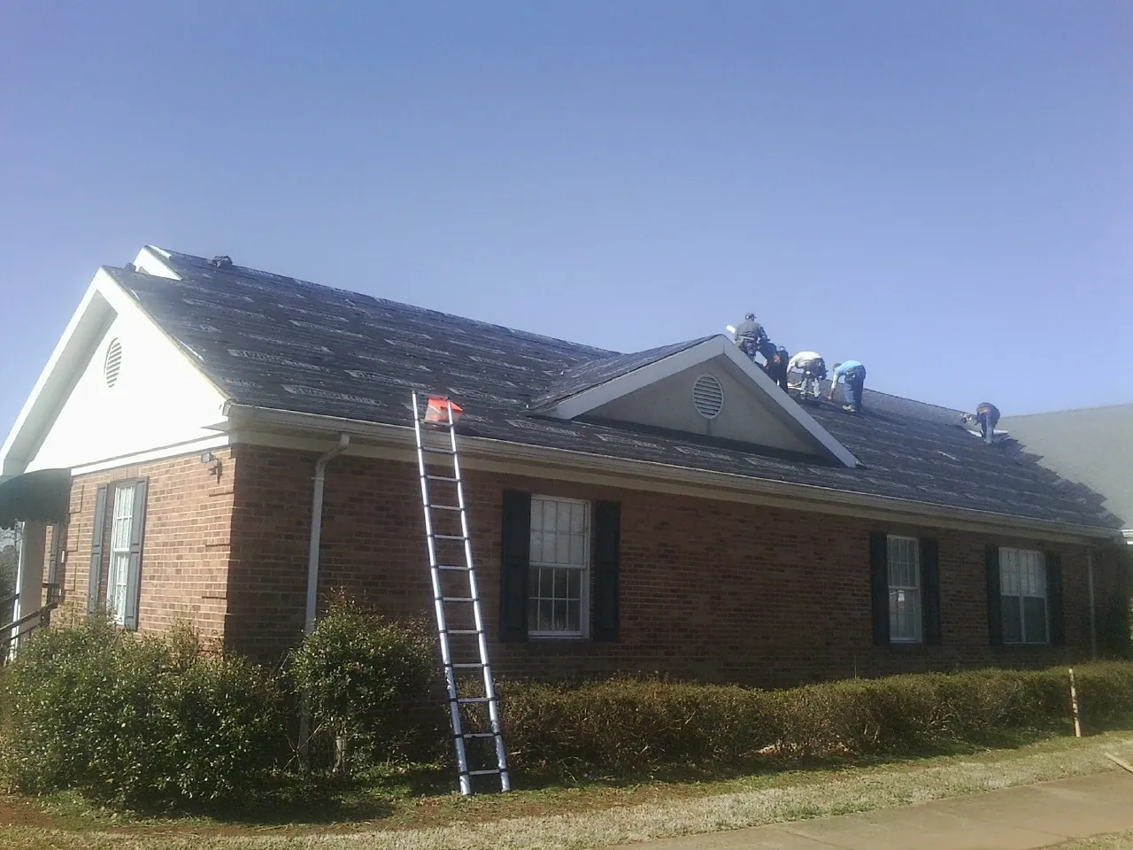 Crew tearing shingles off a brick ranch roof with a ladder set — Metal Roof Repair work by our crew in Penryn