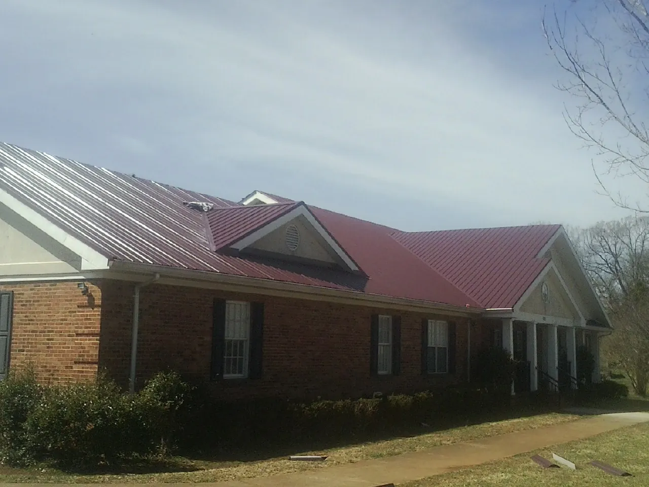 Red metal roof with gabled entries on a long brick building, from a Hail Damage Roof Repair job in Penryn