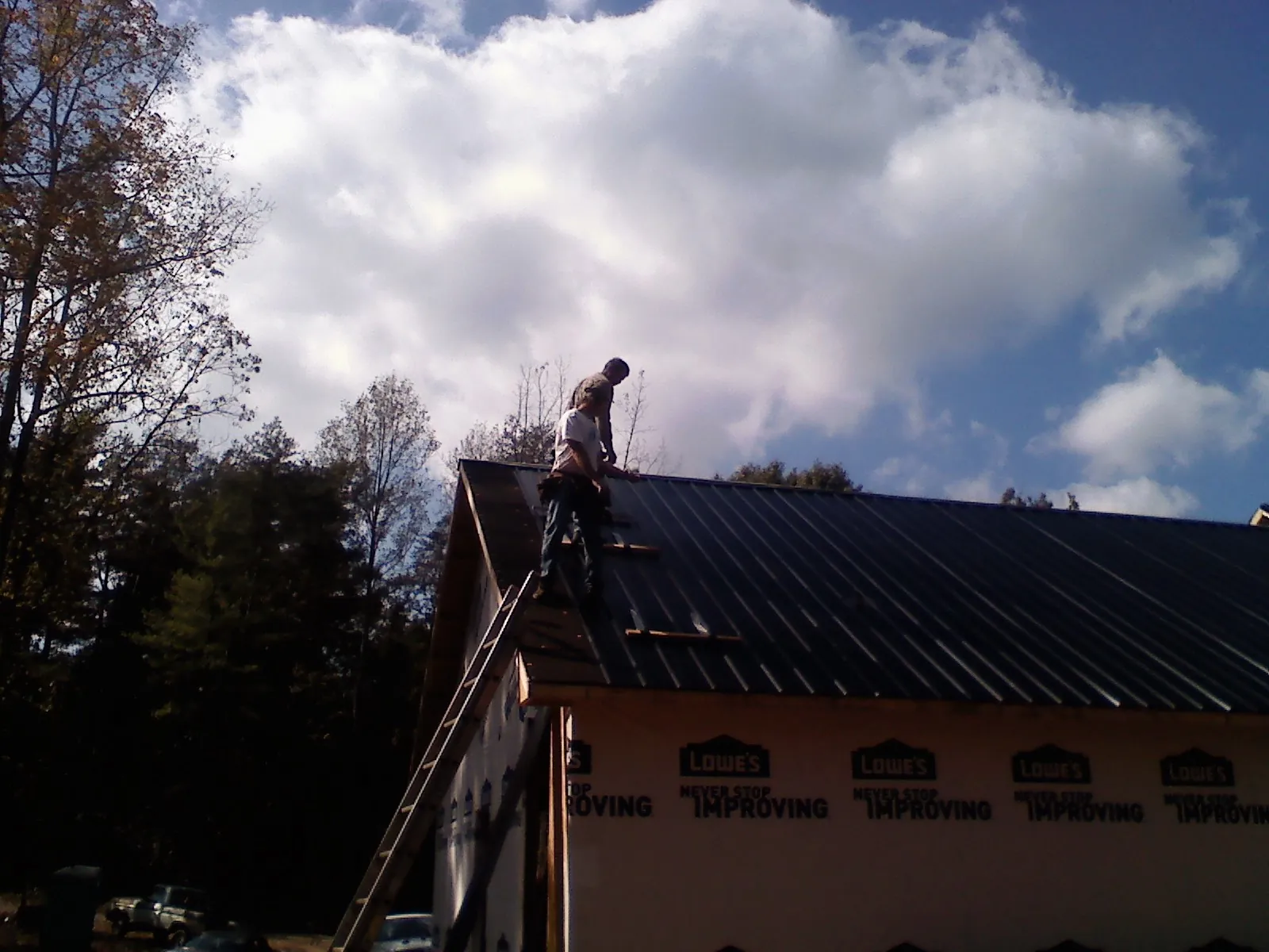 Roofer fastening dark metal panels high against a cloudy sky, from a Roof Inspection job in Penryn