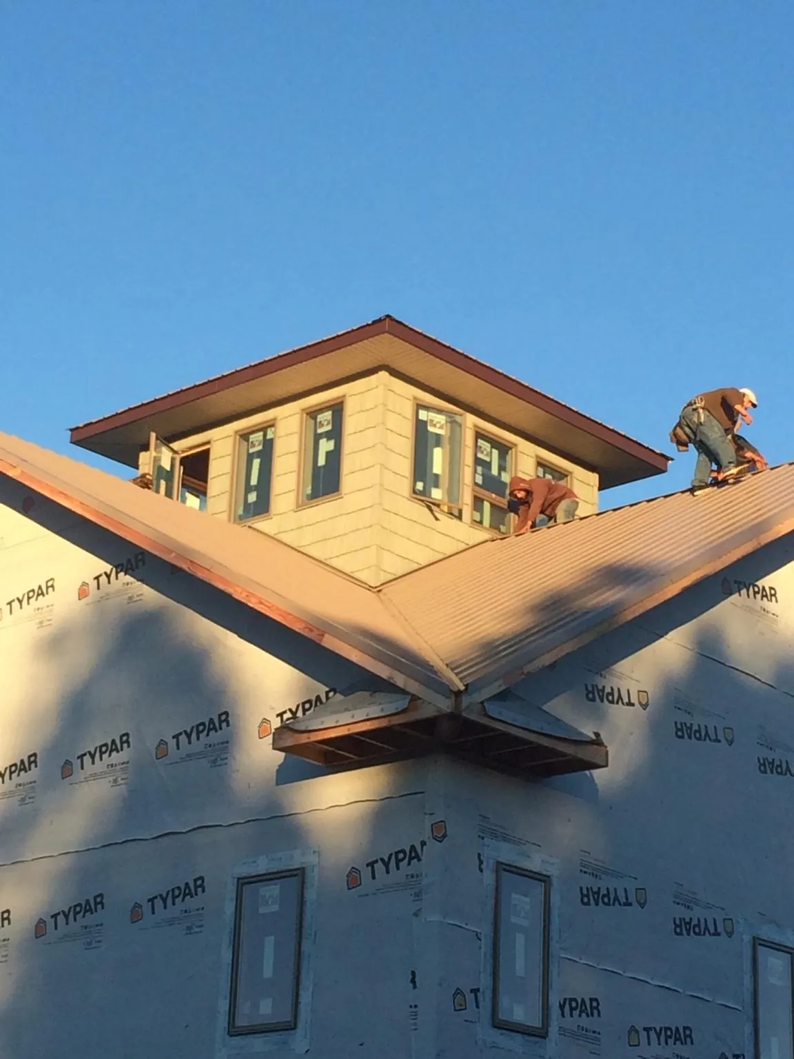 Roofers working around a rooftop cupola on a new metal roof at sunset in Penryn